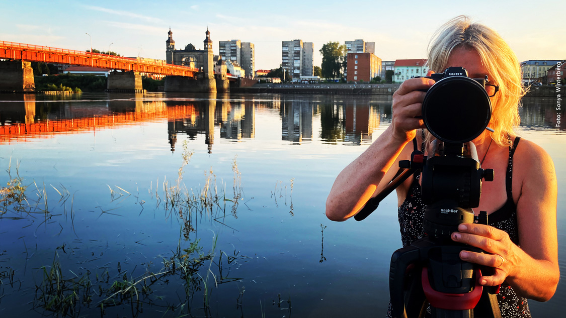  Dreh an der Memel mit Blick nach Russland: Susanne Dzeik mit der Königin-Luise-Brücke und Tilsit/Sowjetsk (Oblast Kaliningrad) im Hintergrund Foto: © Sonya Winterberg